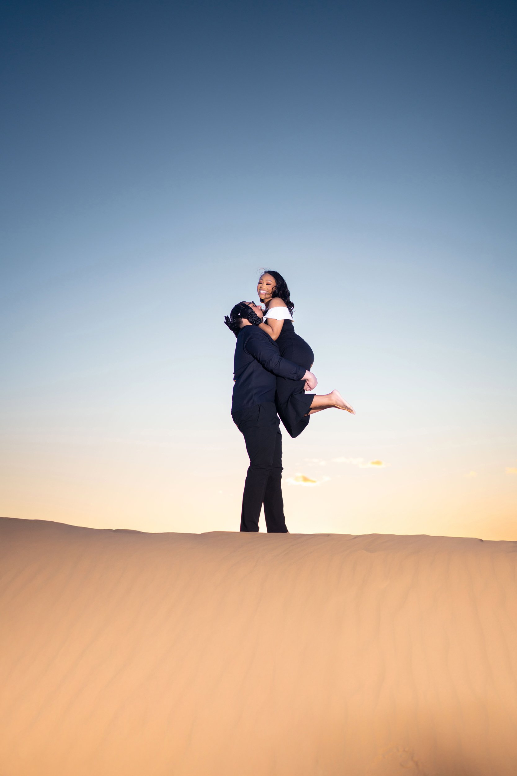 Las Vegas engagement photography — man lifting his fiancee on a sand dune at sunset